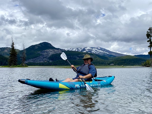 Cory Brown in the Aqua Marina inflatable kayak. He is holding the kayak paddle while wearing a personal flotation device. He is on Sparks Lake in Central Oregon. 