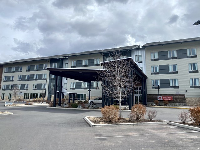 Exterior front entrance to Best Western Premier Peppertree Bend. Four-story hotel in Central Oregon with portico and drive through entrance. A white SUV is parked in front of the hotel, under portico, on a cloudy February day. 