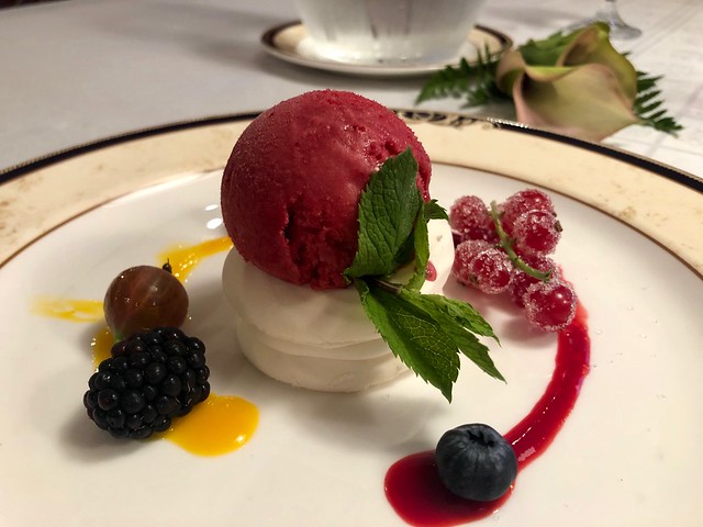 Cloudberry sorbet on meringue with fresh cloudberries dusted in sugar, mint sprig and one blueberry, blackberry and gooseberry.