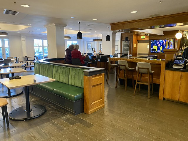 An empty Boxwood Cafe restaurant with two ladies sitting at a table in the bar. Several tables for two people are spread throughout the restaurant on the first floor of the hotel lobby. 