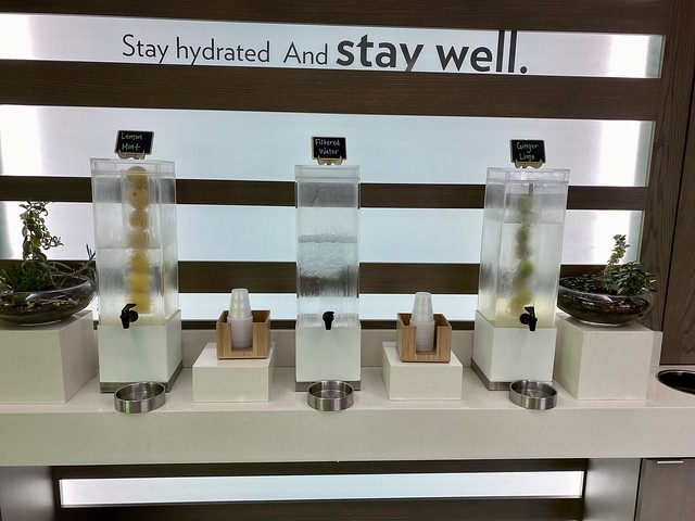 Stay hydrated and stay well sign above three water stations in the Even Eugene hotel lobby. Each of the 3 water stations offers a different flavored water. Cups for hotel guests are along side water coolers. 