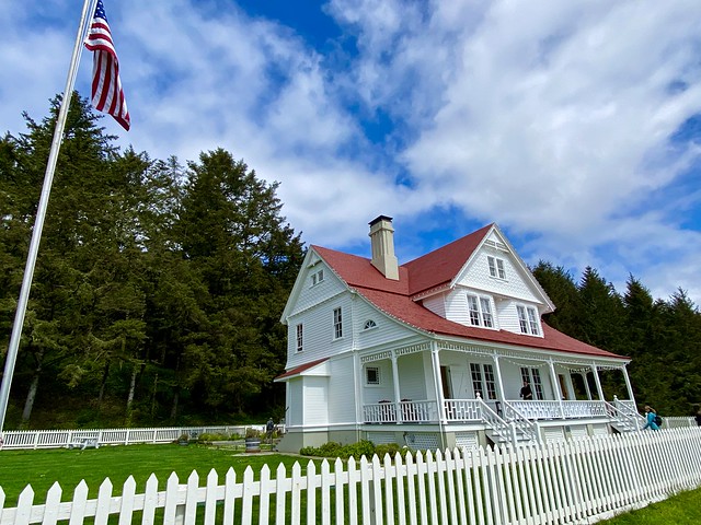 Heceta Lighthouse is a 2-story lightkeeper's cottage in Yachats, Oregon. White house with white picket fence above Pacific Ocean.