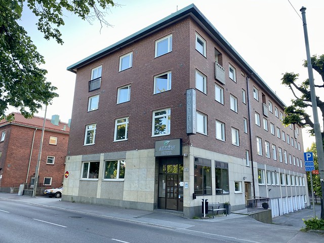 Three-story rectangular Hotel Allen Best Western Gothenburg is a cement and brick building. The front door is on the right of the building with Allen Hotel sign above glass door. Nine square-shaped windows cover the front of the brick hotel. A wire bench is on the side of the building.