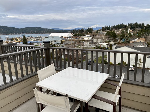 Private rooftop patio from the 5th floor of the Majestic Inn & Spa with Anacortes, Washington and water views. White table and 3 white canvas and wood chairs surround the square table. 