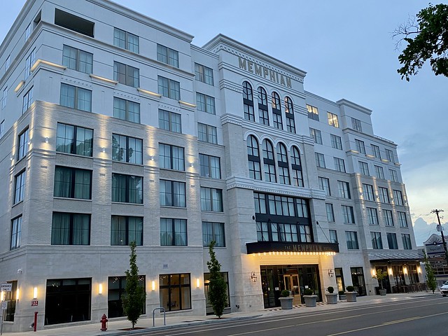 Seven story Memphian Hotel exterior on South Cooper Street at dusk in April. White faux brick and white cement facade with square windows, facing Cooper Street. The Memphian letters are mounted on the top floor of the hotel exterior in mid-town Memphis, Tennessee.