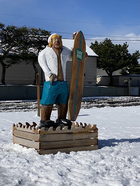 Surfland Hotel wood surfer statue with life-sized wooden surfer and his wooden surfboard. 