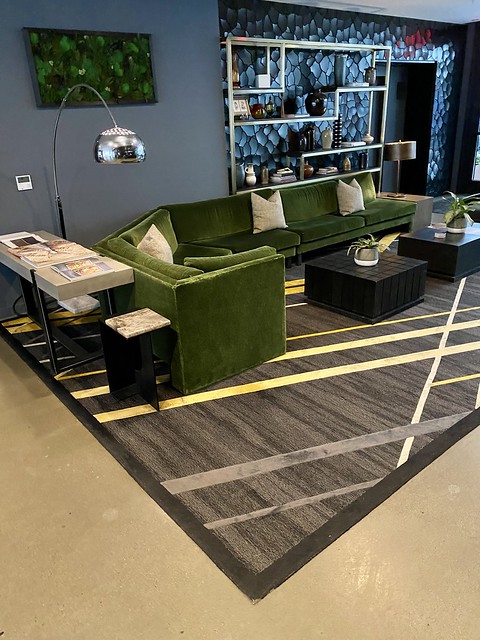 Thompson Seattle hotel lobby with green velvet sectional, modern silver-plated reading lamp arches over sofa. Square black tables are arranged in front of the sofa with one green potted plant on the center of each table. 
