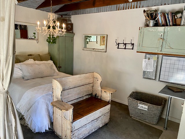Tuscan country cottage is a Monterey Bay Airbnb with queen bed and chandelier hanging from the ceiling. A bench on wheels rests at the foot of the bed. 