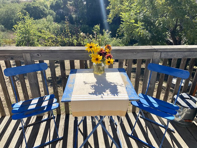 Tuscan Country cottage patio table, with 2 blue chairs and Tuscan flower bouquet on the wood deck in Watsonville, California. 